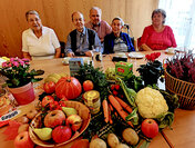 Caritas-Mitarbeiter Olaf Heiduk (hinten) feierte mit Teilnehmer*innen unserer CARENA-Gruppe das Erntedankfest. Die Lebensmittel auf dem Tisch vor ihnen gehen als Spende an den sozialen Mittagstisch des Guten Hirten.
