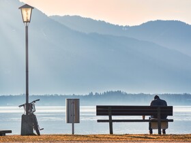 Person sitzt alleine auf einer Parkbank an einem See 