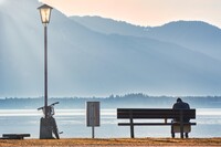 Person sitzt alleine auf einer Parkbank an einem See 